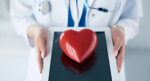 Doctora con estetoscopio sosteniendo el corazón, sobre fondo claro — Foto de Stock