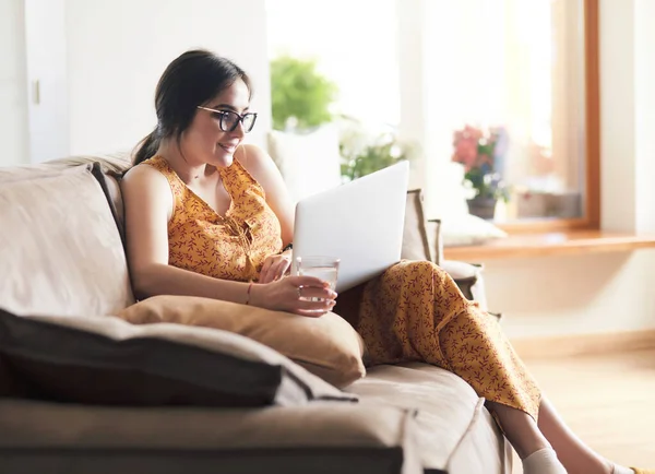 Evde dizüstü bilgisayar üzerinde çalışan kanepede oturan genç kadın — Stok fotoğraf