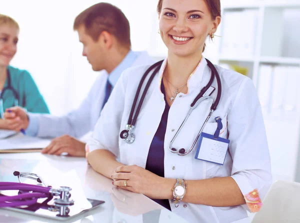 Bonito jovem sorridente médico feminino sentado na mesa — Fotografia de Stock