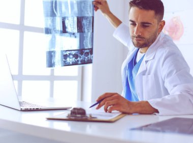 Yakışıklı doktor genç bayan hastasıyla konuşuyor ve ofisinde otururken notlar alıyor..