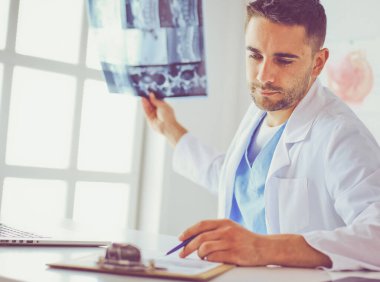 Genç doktor ofisinde oturuyor ve röntgen sonuçlarını inceliyor.