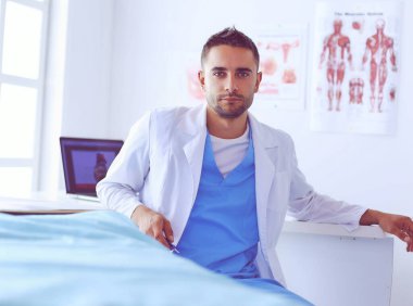 Yakışıklı doktor genç bayan hastasıyla konuşuyor ve ofisinde otururken notlar alıyor..