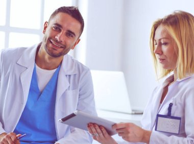 Yakışıklı doktor genç bayan doktorla konuşuyor ve ofisinde otururken notlar alıyor..