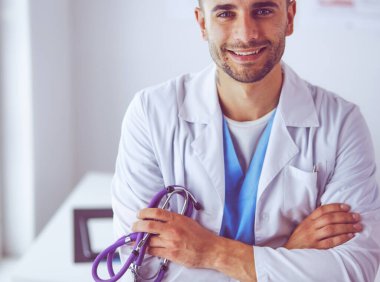 Genç ve kendinden emin erkek doktor portresi tıp ofisinde duruyor..