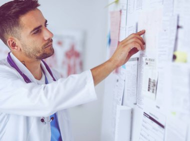 Genç ve kendinden emin erkek doktor portresi tıp ofisinde duruyor.