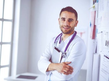 Genç ve kendinden emin erkek doktor portresi tıp ofisinde duruyor.