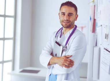 Genç ve kendinden emin erkek doktor portresi tıp ofisinde duruyor..