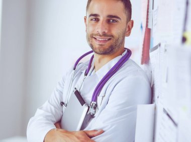 Genç ve kendinden emin erkek doktor portresi tıp ofisinde duruyor.