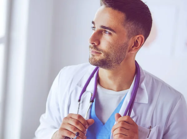 Retrato médico masculino joven y confiado de pie en el consultorio médico. — Foto de Stock