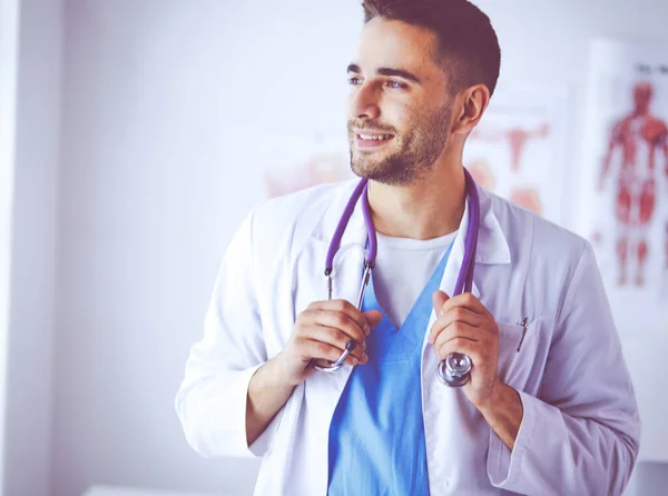 Retrato médico masculino joven y confiado de pie en el consultorio médico — Foto de Stock