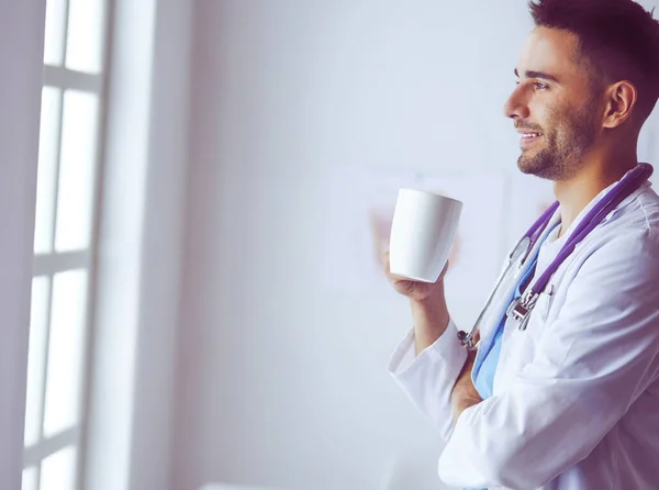 Young doctor with coffee cup in medical office