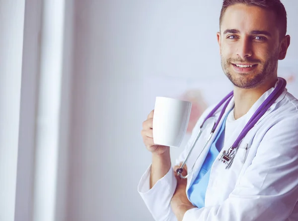 Young doctor with coffee cup in medical office — Stock Photo, Image