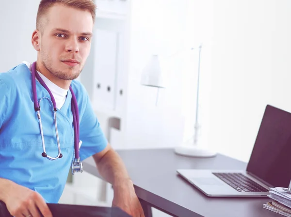 Ritratto di un medico maschio sorridente con computer portatile seduto alla scrivania nello studio medico — Foto Stock