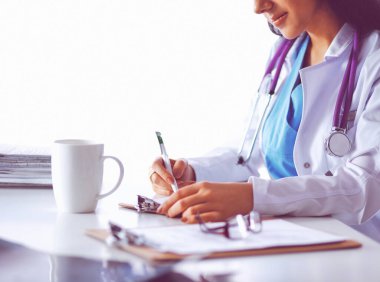 Kadın doktor elinde kağıtlarla masada oturuyor ve çalışıyor.