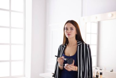 Makyaj fırçası yüzüne yakın bir kadın portresi.