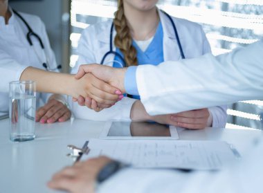 Doktor beyaz arka planda izole edilmiş bir hastayla el sıkışıyor.