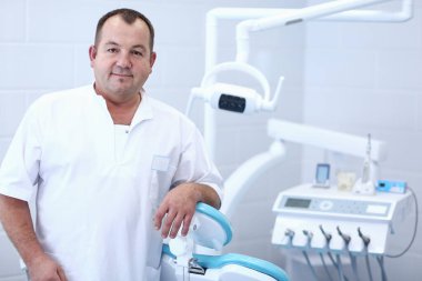 Diş kliniğinde duran gülümseyen bir dişçinin portresi.