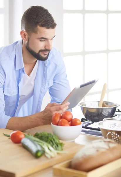 Hombre siguiendo la receta en la tableta digital y cocinar comida sabrosa y saludable en la cocina en casa — Foto de Stock