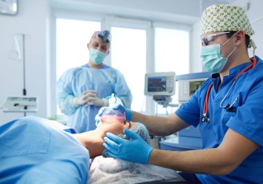 Ameliyat odasında arka planda erkek cerrah var.