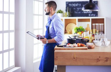 Dijital tablet ve yemek pişirme tarifine uyan bir adam evdeki mutfakta lezzetli ve sağlıklı yemekler pişiriyor.