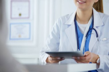 Kadın doktor hastane lobisinde tablet bilgisayar kullanarak, gülümseyerek
