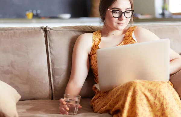 Красива молода жінка сидить на дивані і працює на ноутбуці — стокове фото