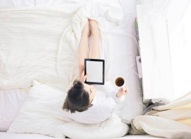 Sabahları yatakta otururken tablet kullanan ve kahve içen kadın portresi