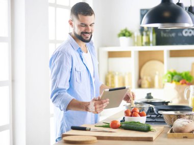Dijital tablet ve yemek pişirme tarifine uyan bir adam evdeki mutfakta lezzetli ve sağlıklı yemekler pişiriyor.
