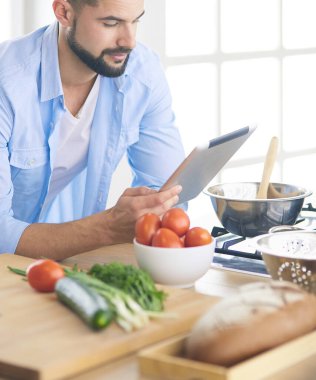 Dijital tablet ve yemek pişirme tarifine uyan bir adam evdeki mutfakta lezzetli ve sağlıklı yemekler pişiriyor.
