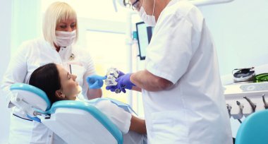 Genç bayan hastayı muayene eden ve üzerinde çalışan erkek dişçiler. Diş hekimliği..