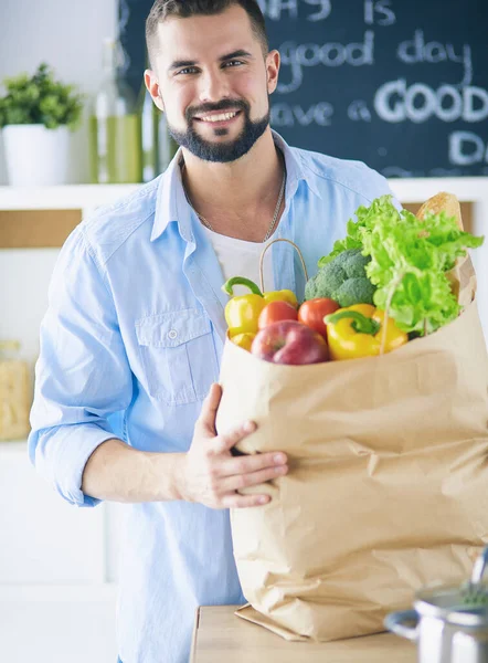 Man holding paper bag full of groceries on the kitchen background. Shopping and healthy food concept