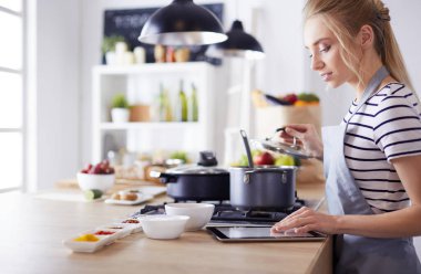 Mutfakta yemek yapmak için tablet bilgisayar kullanan genç bir kadın.