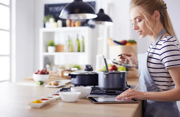 Mujer joven usando una tableta para cocinar en su cocina —  Fotos de Stock