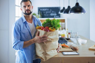 Mutfak arka planında poşet dolusu erzak tutan adam. Alışveriş ve sağlıklı gıda konsepti