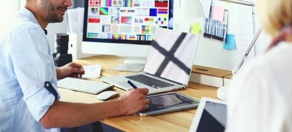 Retrato del joven diseñador sentado en el estudio gráfico frente a la computadora portátil y el ordenador mientras trabaja en línea. — Foto de Stock