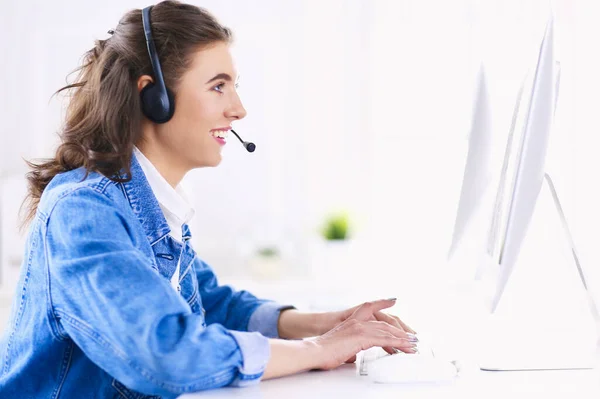 Feliz encantadora joven sentada y trabajando con el ordenador portátil con auriculares en la oficina — Foto de Stock