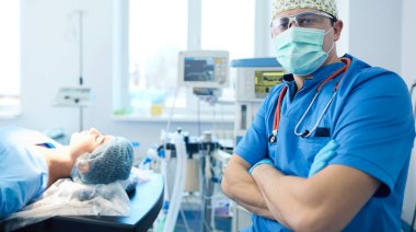 Ameliyat odasında arka planda erkek cerrah var.