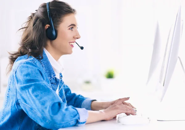 Heureuse charmante jeune femme assise et travaillant avec un ordinateur portable en utilisant un casque dans le bureau — Photo