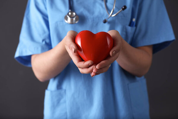 Doctor with stethoscope holding heart, isolated on gray background