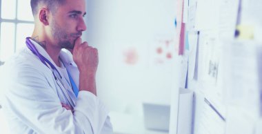 Genç ve kendinden emin erkek doktor portresi tıp ofisinde duruyor..