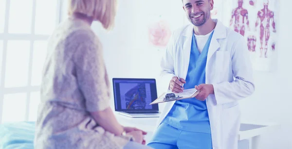 Schöner Arzt spricht mit junger Patientin und macht sich Notizen, während er in seinem Büro sitzt. — Stockfoto