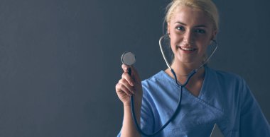 Steteskopla dinleyen kadın doktor, gri arka planda izole edilmiş.