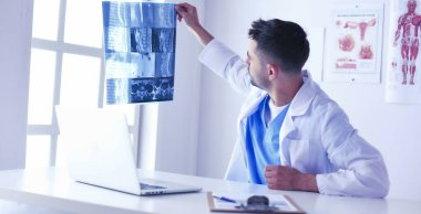 Genç doktor ofisinde oturuyor ve röntgen sonuçlarını inceliyor.
