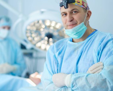 Ameliyat odasında arka planda erkek cerrah var.