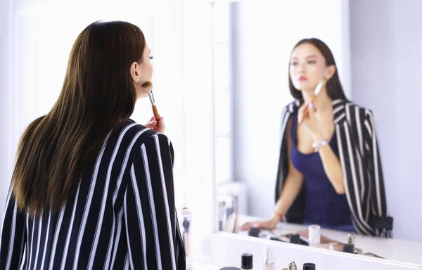 Vacker flicka tittar i spegeln och tillämpa kosmetika med en stor borste — Stockfoto