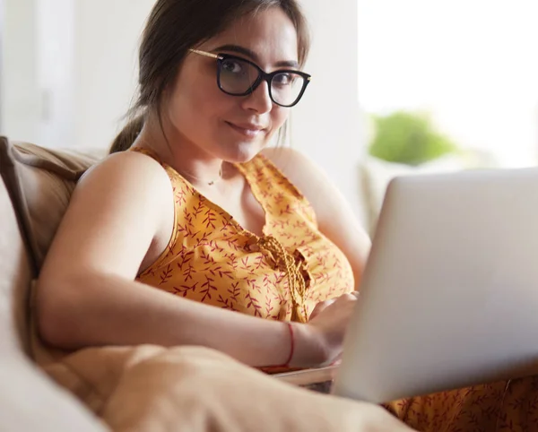 Молодая женщина сидит на диване, работая на ноутбуке дома — стоковое фото