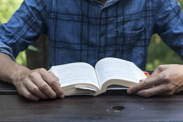 Άνθρωπος Που Διαβάζει Ένα Βιβλίο Ένα Ξύλινο Τραπέζι Κήπου — Φωτογραφία Αρχείου