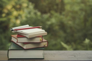Bahçe ahşap bir masa üzerinde kitap yığını, yeşil doğa arka planı 