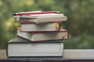 Eski kitap yığını, not defteri ve tahta bir bahçe masasında kalem.,