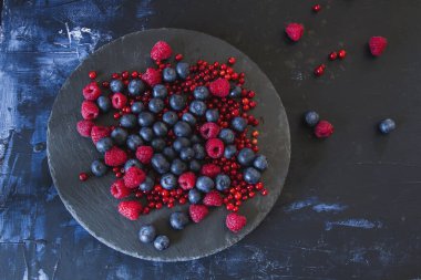 Yaban mersini, kırmızı üzümler ve ahududu meyveleri siyah bir levhada